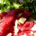 Bresaola su un tagliere di legno, con fette sottili e contorni di rucola e limone.