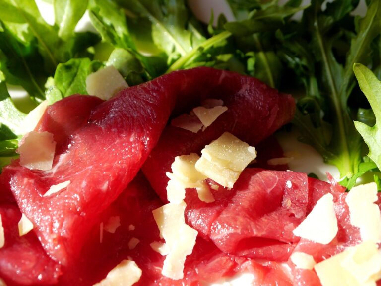 Bresaola su un tagliere di legno, con fette sottili e contorni di rucola e limone.