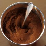 Immagine di una tazza di caffè decaffeinato in polvere con chicchi di caffè sullo sfondo.