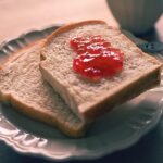 Immagine di una fetta di pane su un tavolo, con un misuratore di glicemia e un piatto di cibo sano accanto.